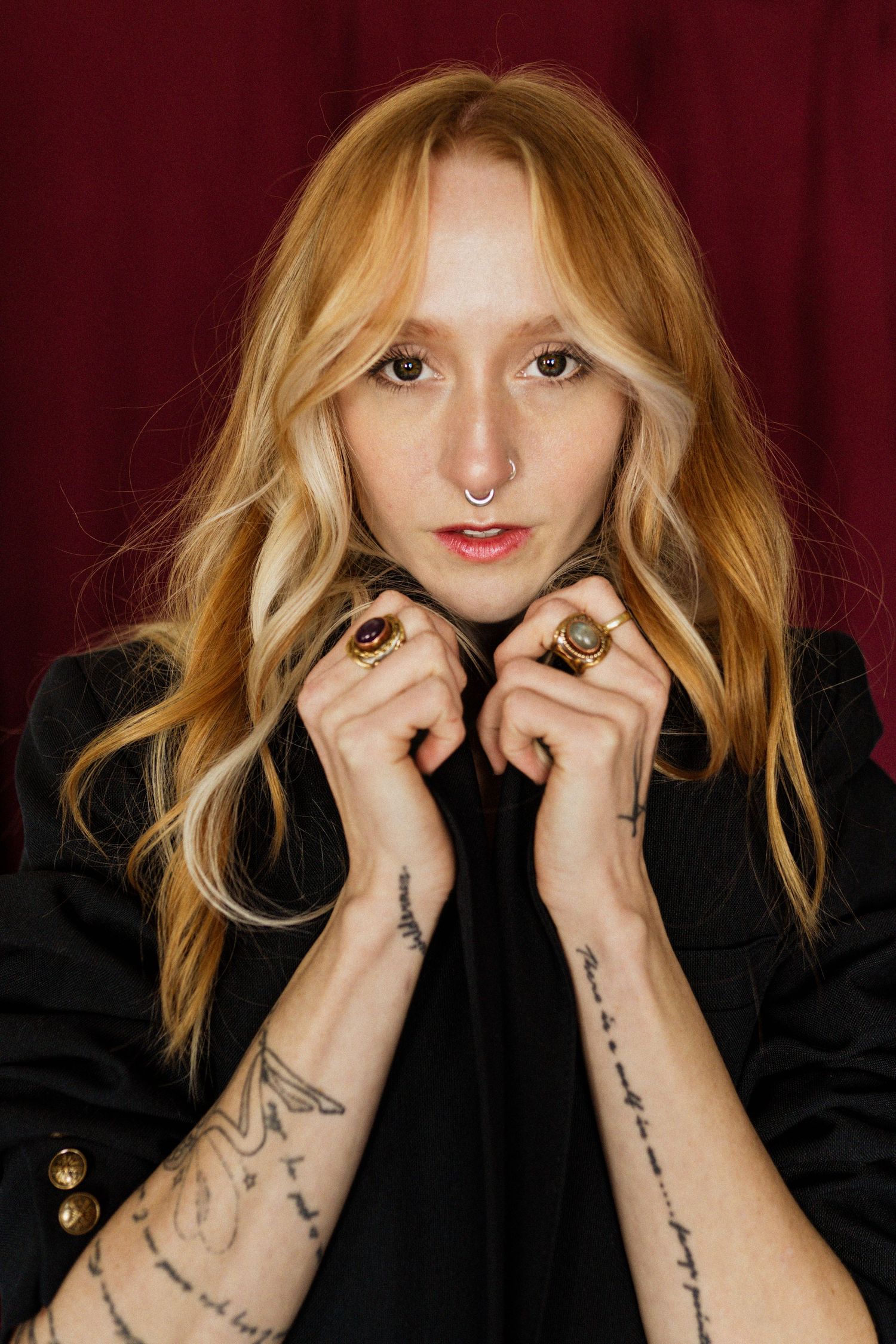 A young woman with red nails and lips in a white shirt poses thoughtfully against a dark background.