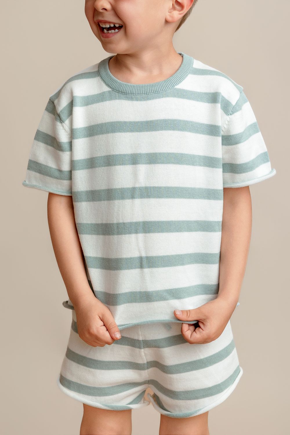 Smiling toddler boy wearing a sage green and white striped knit t-shirt and matching shorts set.
