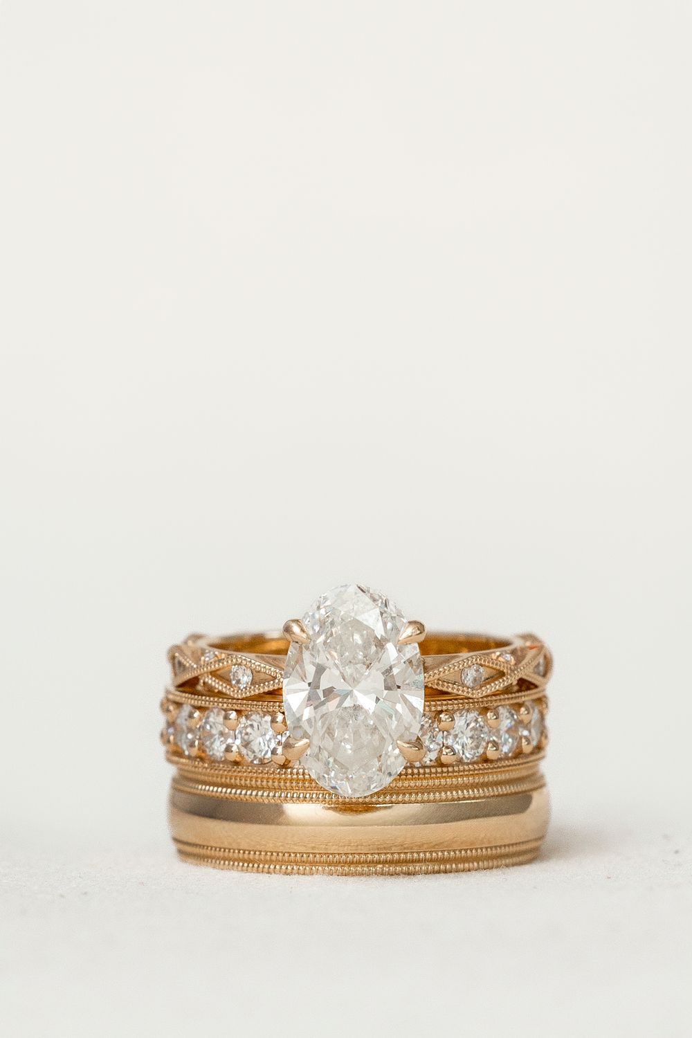 Gold oval diamond solitaire engagement ring stacked with diamond eternity and milgrain wedding bands.