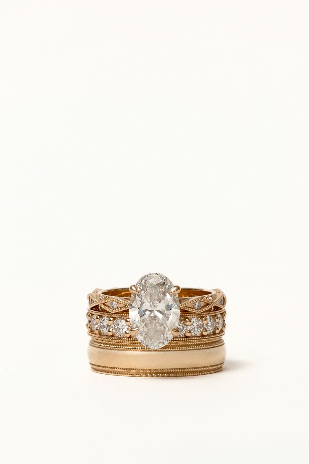 Stacked gold rings featuring an oval diamond solitaire with milgrain and diamond band details.