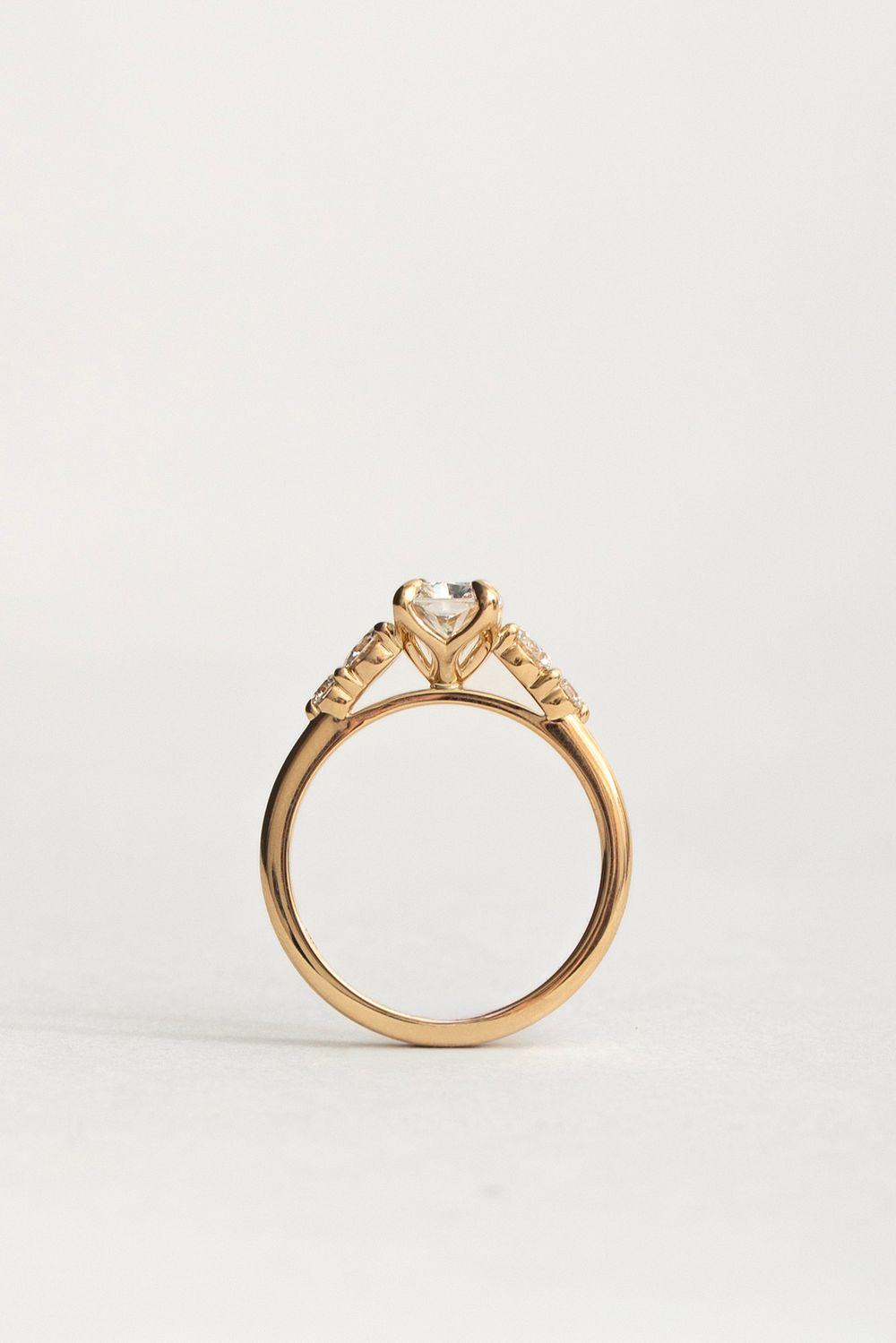 Gold engagement ring with a round diamond center stone and accent diamonds on the band, photographed on white background.