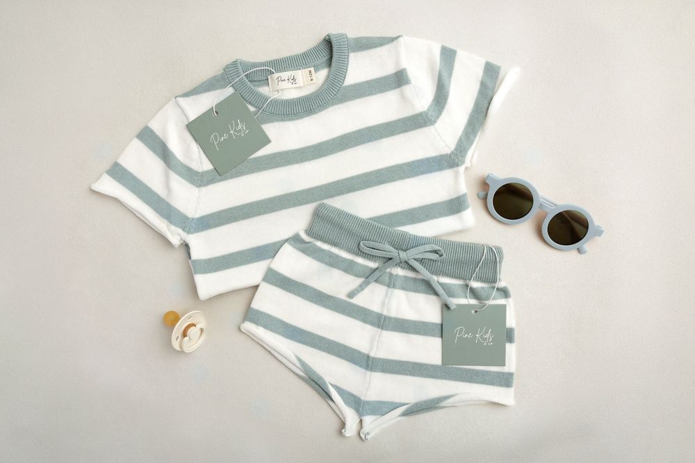 Baby blue and white striped knit top and shorts set displayed flat with sunglasses and pacifier on white background.