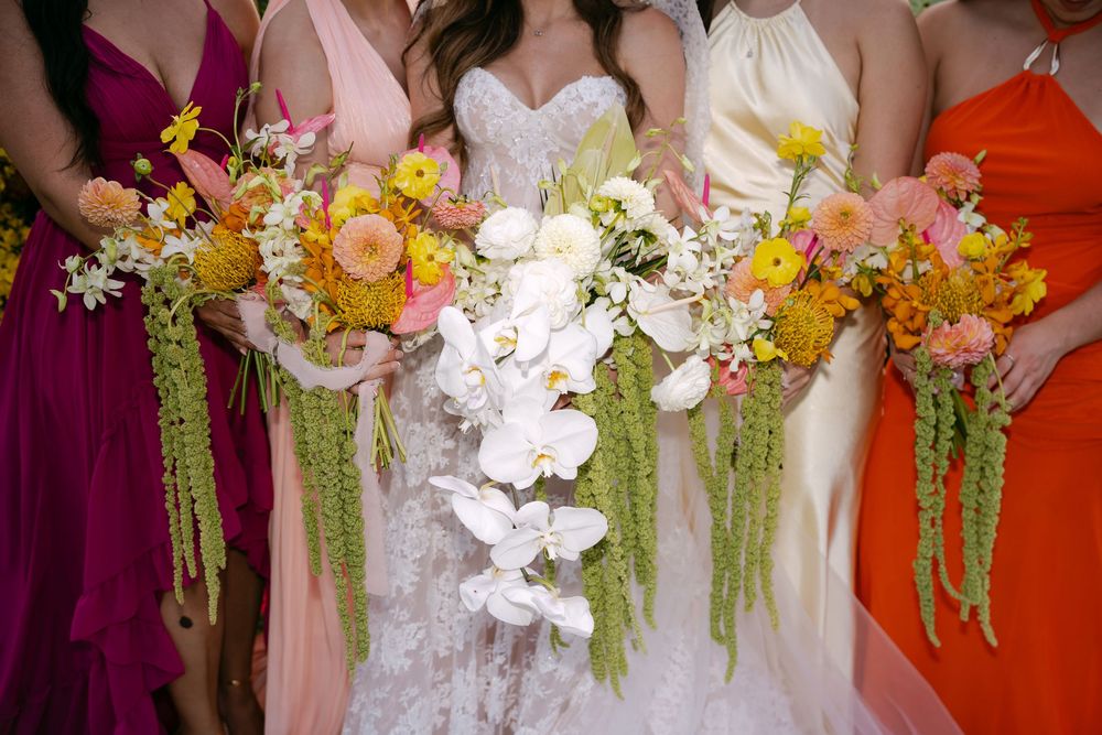 Bride and bridesmaids holding colorful cascading bouquets with white orchids, yellow flowers, and green amaranthus.