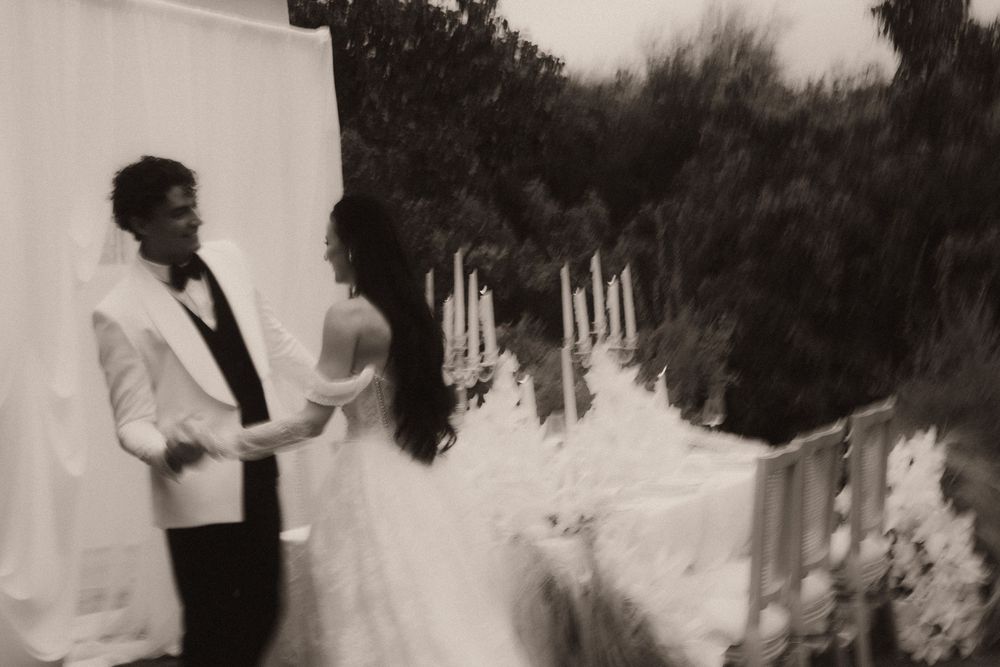 Black and white photo of a bride and groom holding hands during an outdoor wedding ceremony.