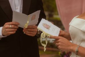 Bride and groom exchanging wedding vows, holding ceremony booklets during outdoor wedding ceremony.