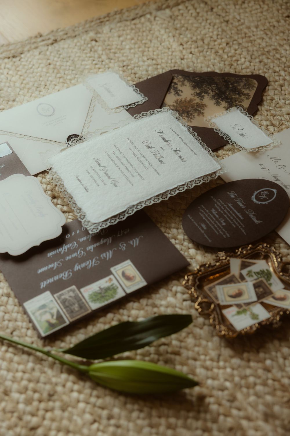 Elegant wedding stationery suite with brown and cream tones, lace details, envelopes, and botanical stamps on textured burlap.