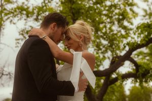 Bride and groom share an intimate moment outdoors, surrounded by lush green trees on their wedding day.
