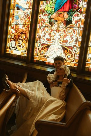 Bride and groom share a romantic moment in a church pew beneath stunning stained glass windows.