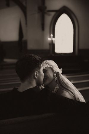 Black and white photo of a bride and groom sharing an intimate moment in a church pew.