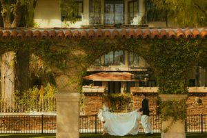 Bride and groom pose under ivy-covered stone arch at elegant outdoor wedding venue.