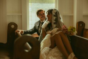 A joyful bride and groom share a candid moment sitting together in a church pew on their wedding day.