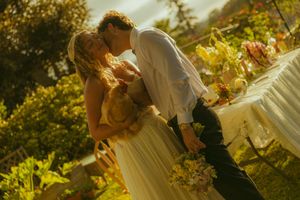 A bride and groom share a romantic kiss outdoors at their garden wedding ceremony in warm golden sunlight.