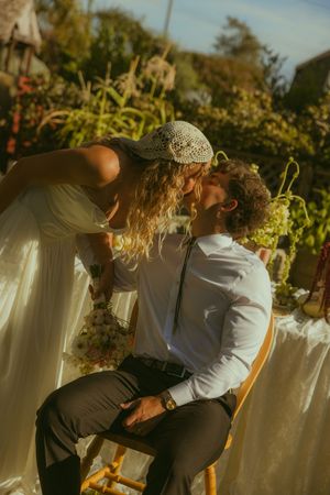 A bride and groom share a romantic kiss outdoors at a garden wedding reception in warm golden light.