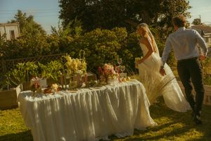 Bride and groom walking toward a floral decorated wedding table outdoors in a sunlit garden setting.