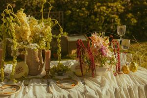 Elegant outdoor tablescape with lush floral arrangements, candles, and draped linens in warm golden light.