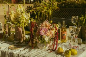 Elegant outdoor tablescape with floral centerpieces, pears, wine glasses, and a bottle in warm golden sunlight.