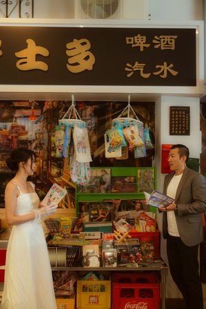 Couple in wedding attire browsing a vintage Hong Kong convenience store with Chinese signage and retro merchandise displays.