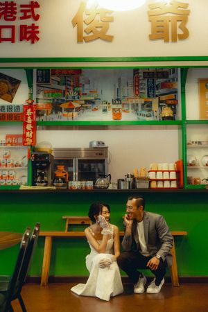 Couple in wedding attire sitting together at a Hong Kong-style cafe with green decor and Chinese signage.