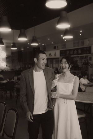 Black and white photo of a smiling couple in a restaurant, man in blazer and woman in white dress.