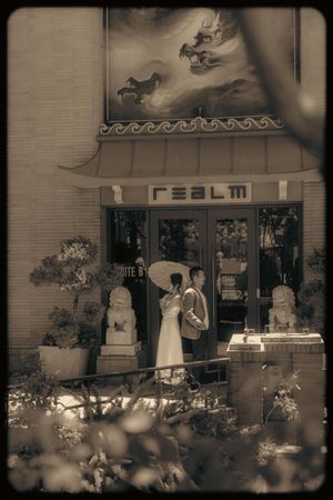 Sepia-toned photo of a couple in wedding attire outside the Realm restaurant with Asian-inspired decor.