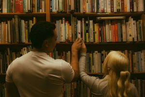Two people browsing colorful books on wooden library shelves in a cozy bookstore setting.