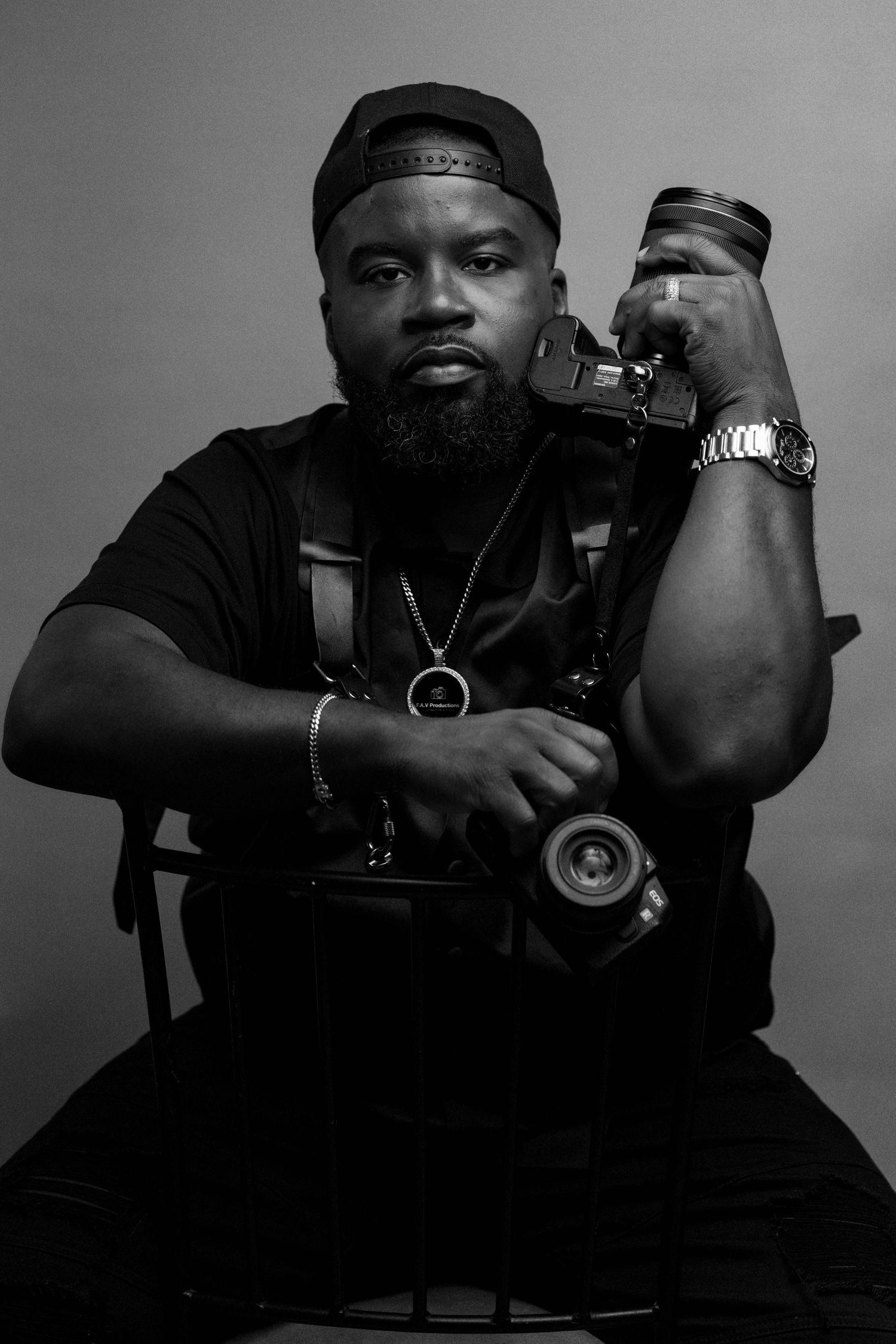 Black and white portrait of a bearded man in a suit holding a professional camera rig on his shoulder.