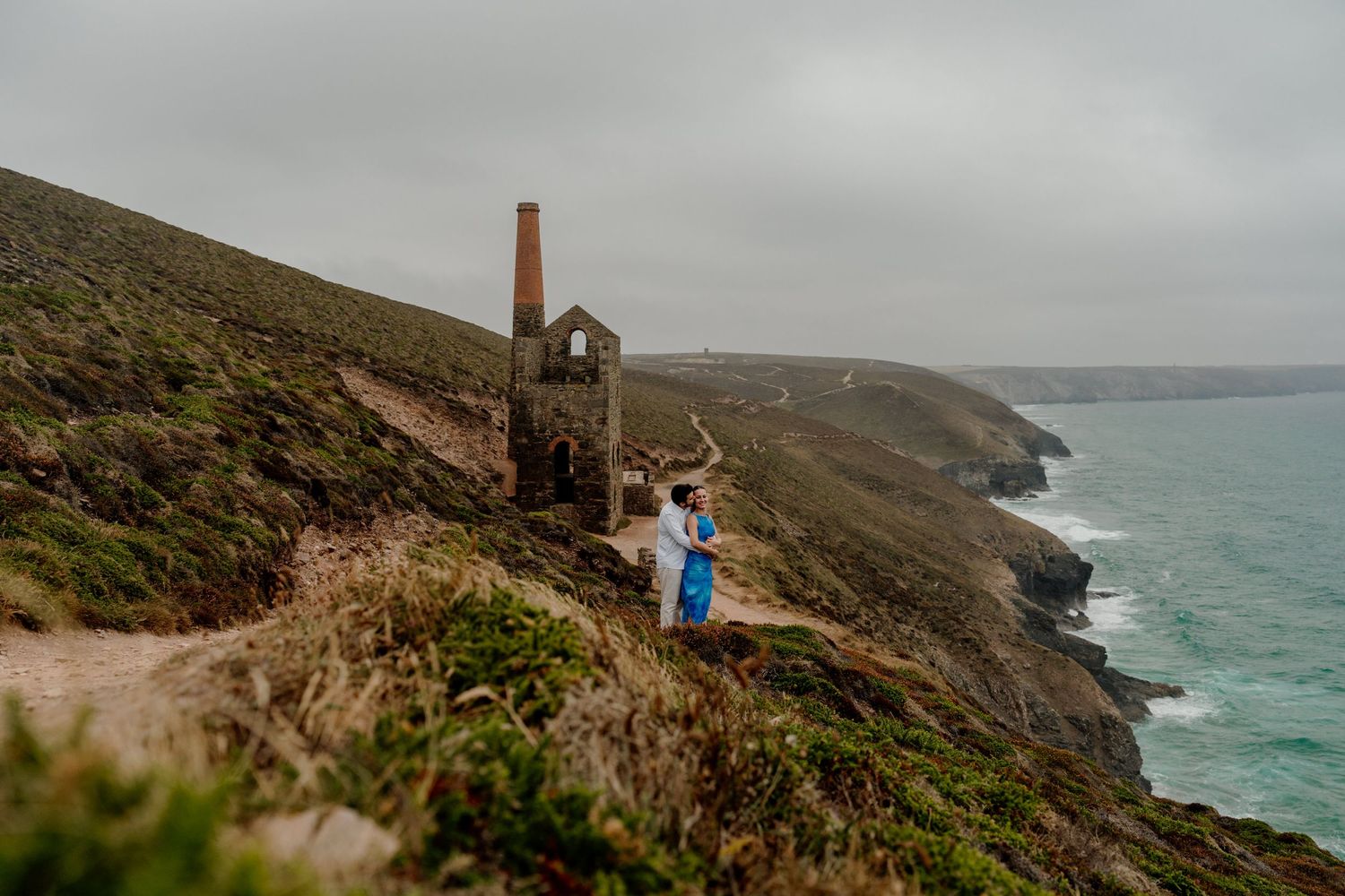 Couple embracing near historic Wheal Coates tin mine ruins on dramatic Cornwall clifftop with turquoise sea views.