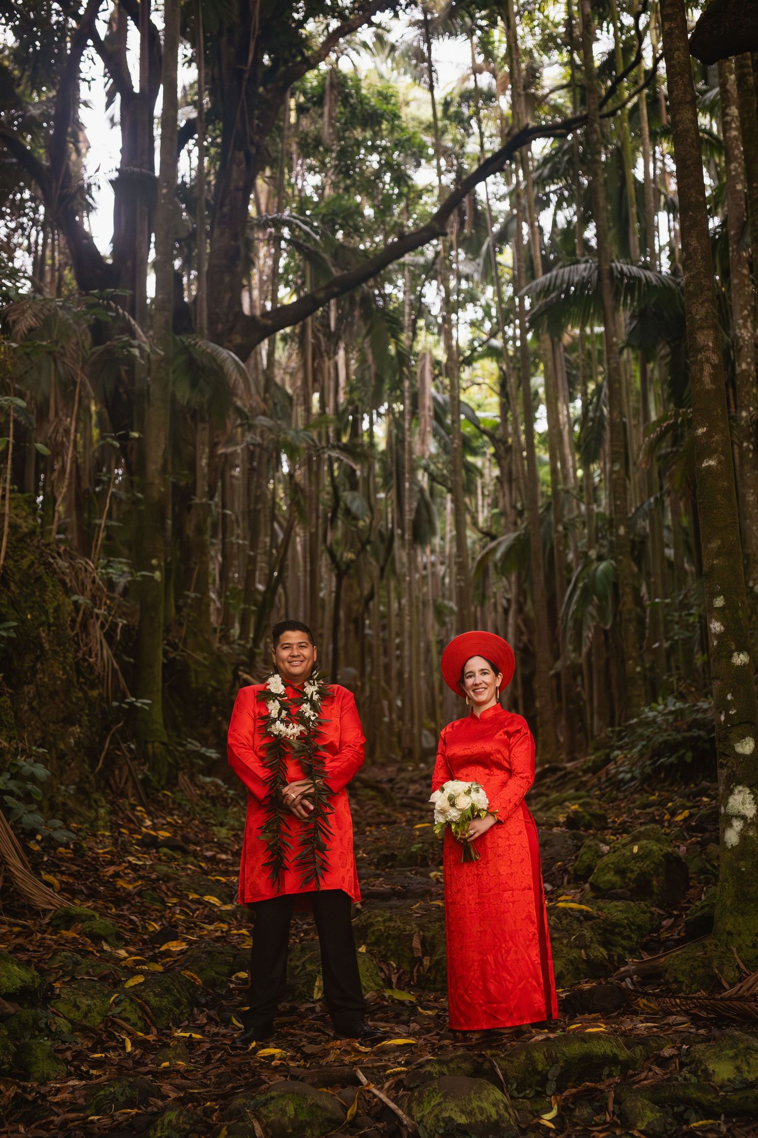 Couple in traditional Vietnamese red ao dai wedding attire stand in lush tropical forest.  Hawaii Jungle Elopement.