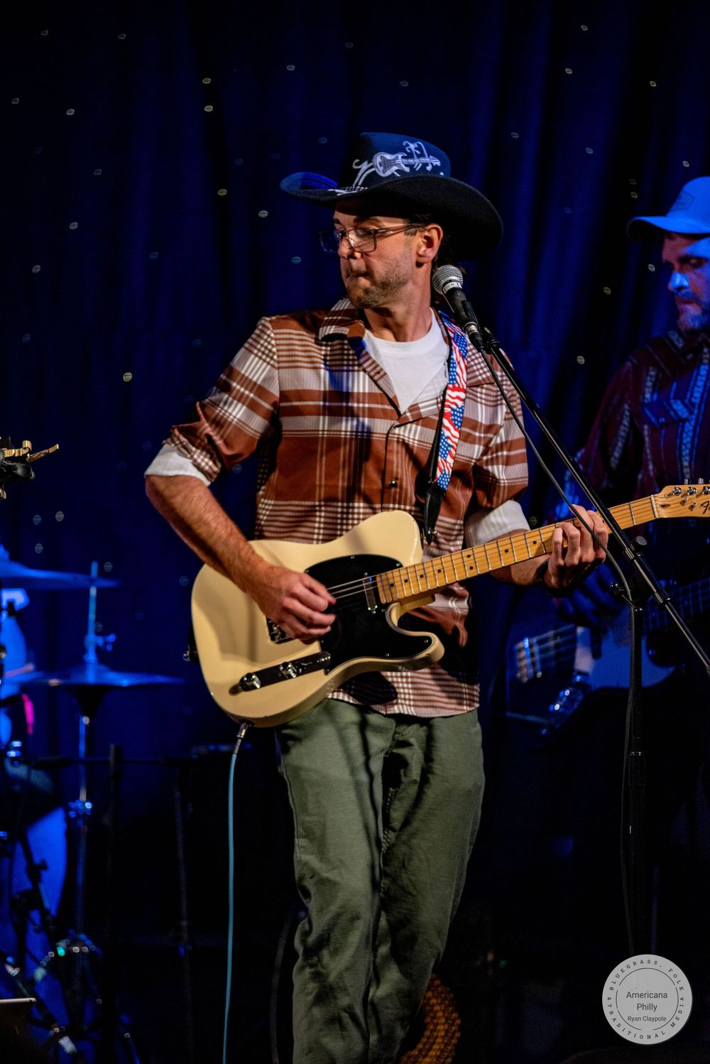 Musician in cowboy hat plays Fender Telecaster guitar on stage in plaid shirt at live country music performance.