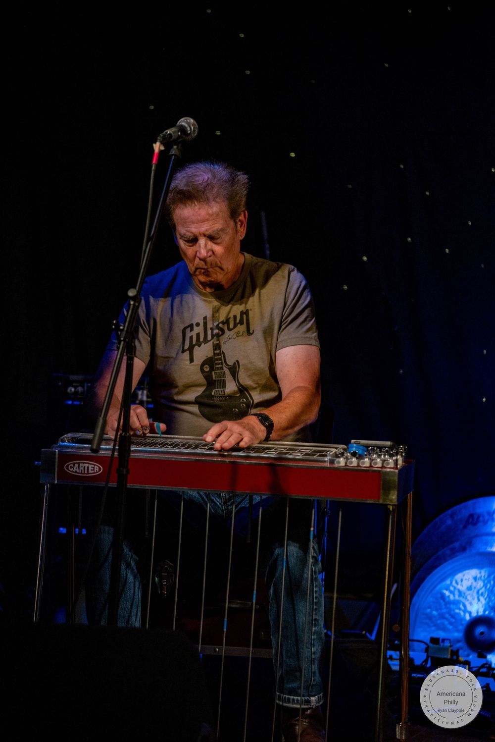 Musician playing a pedal steel guitar on stage, wearing a Gibson t-shirt, performing under stage lights.