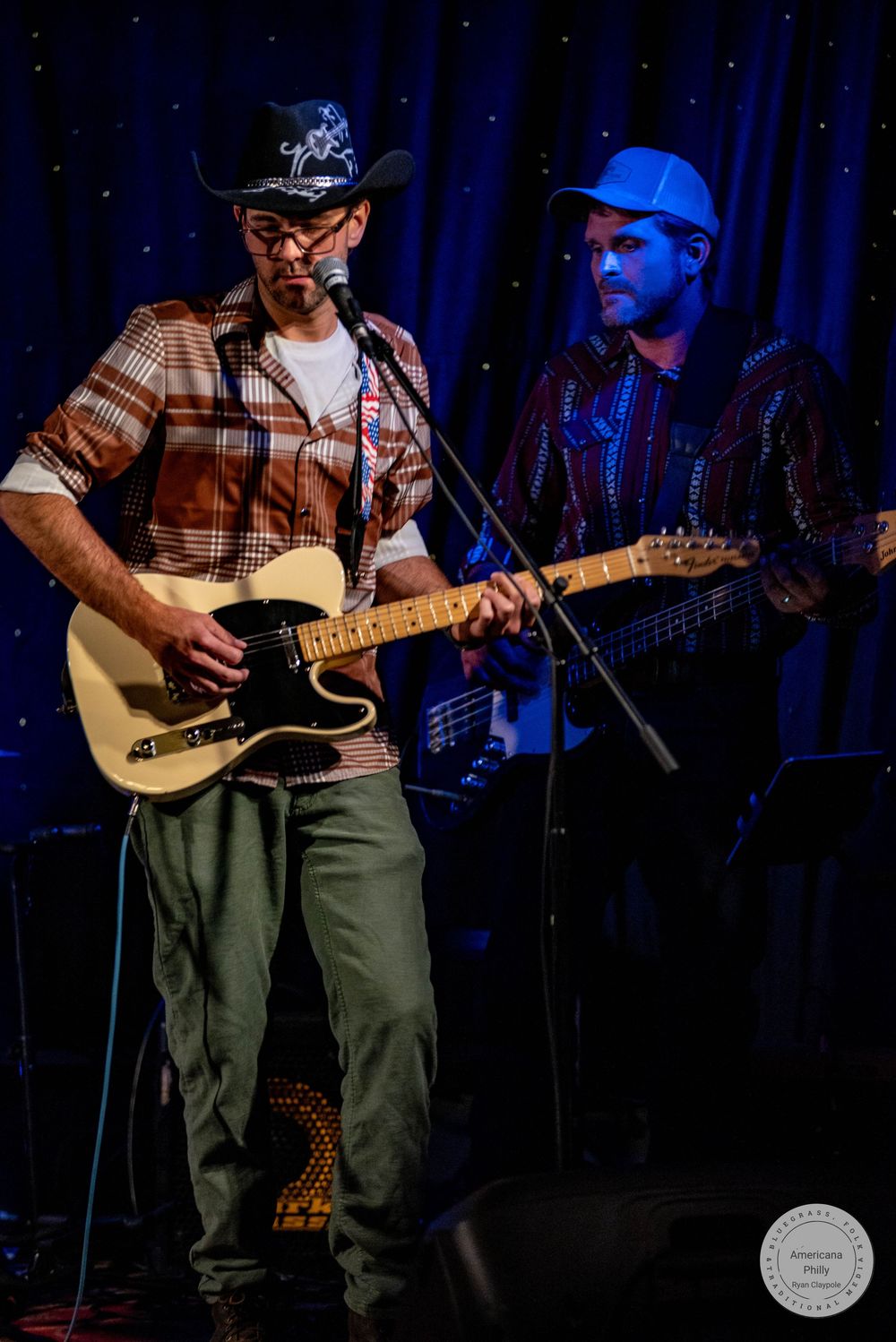 Two musicians performing live, one playing a cream Telecaster guitar wearing a cowboy hat, another playing electric guitar on stage.