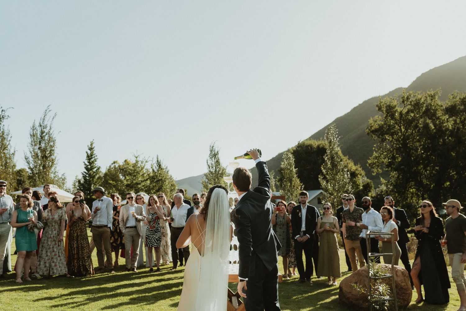 Black and white wedding photo of couple walking through confetti shower surrounded by cheering guests.