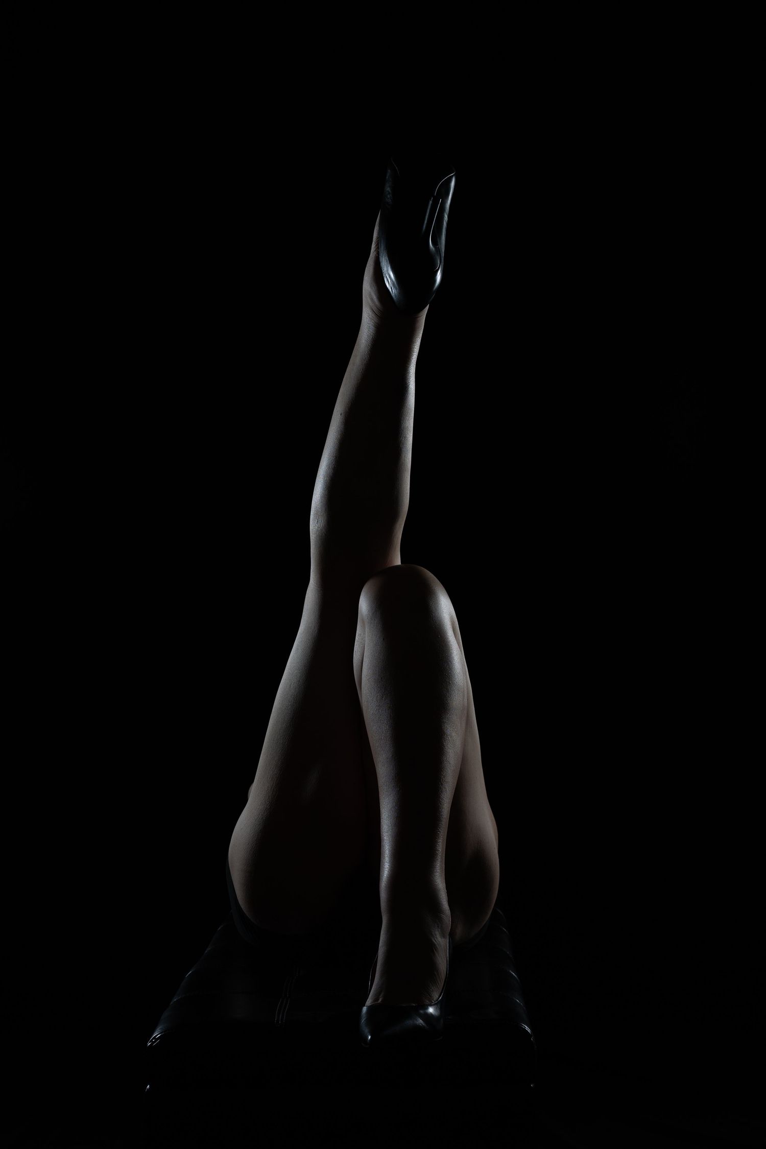 Silhouette of elegant legs raised against black background, dramatic low-key lighting highlighting feminine form.