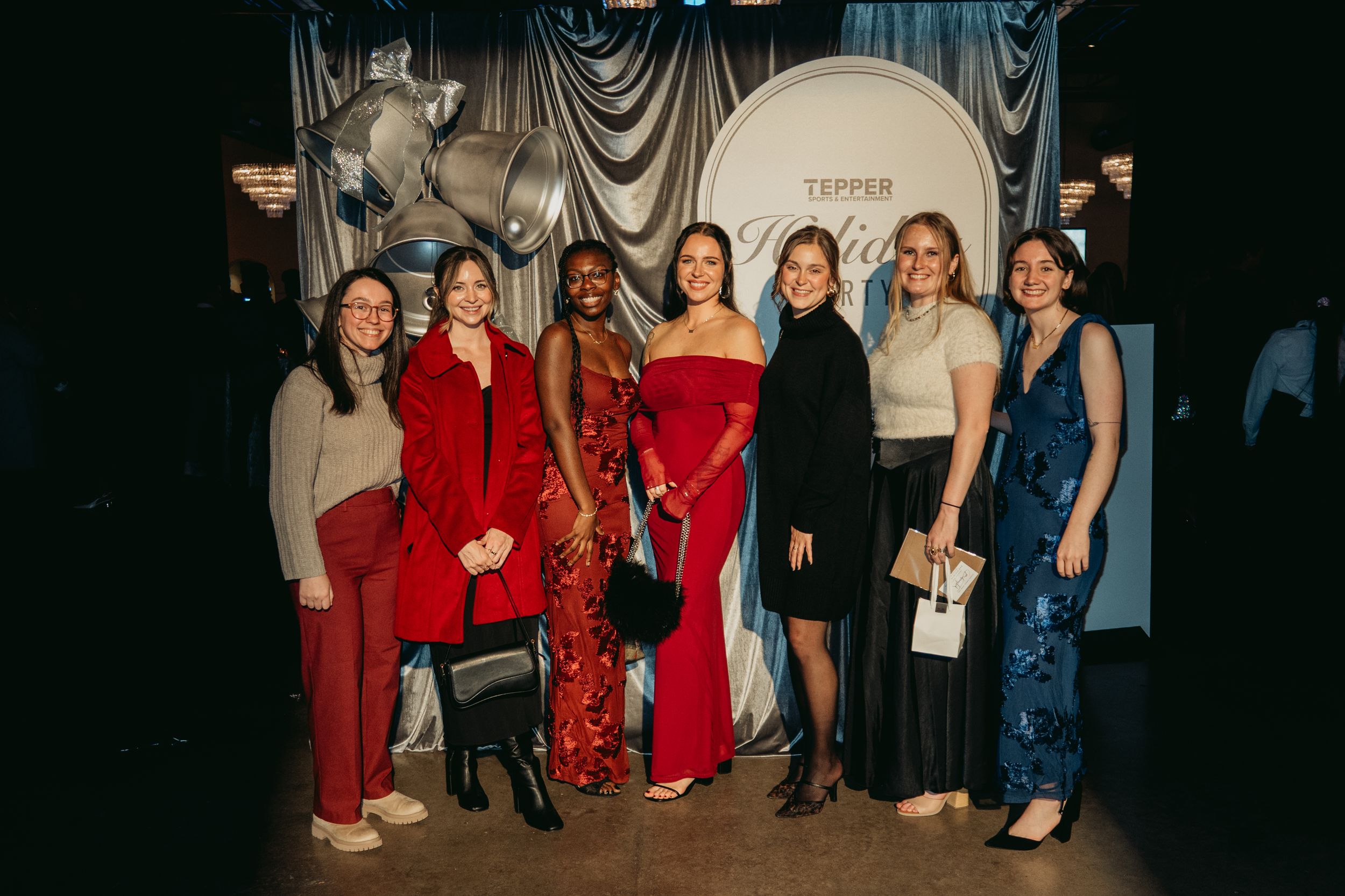 Seven women posing together at a formal event in front of a Tepper backdrop, wearing elegant dresses.