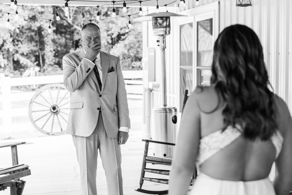 Emotional father sees bride daughter for first time on wedding day in black and white photo at rustic barn venue.