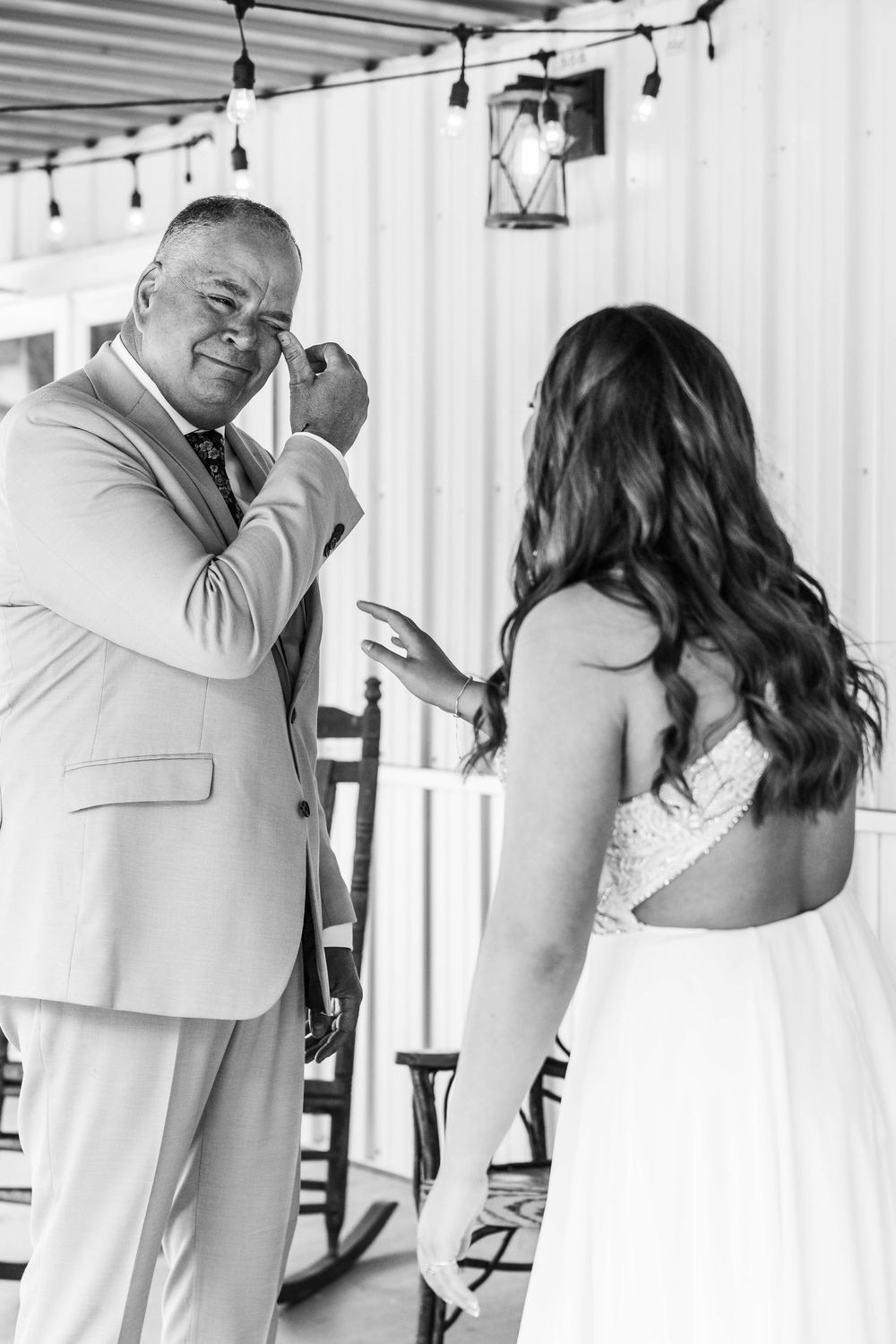 Emotional father sees bride daughter for first time on wedding day, wiping tears in black and white photo.