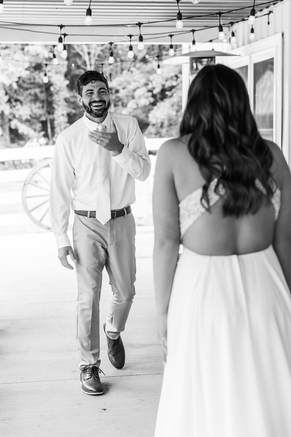 Black and white photo of groom smiling at bride during first look at rustic outdoor wedding venue.