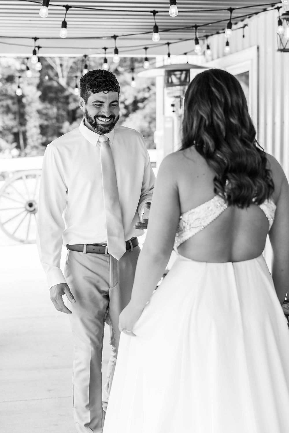 Black and white photo of a groom smiling at his bride during a first look at a rustic barn wedding venue.