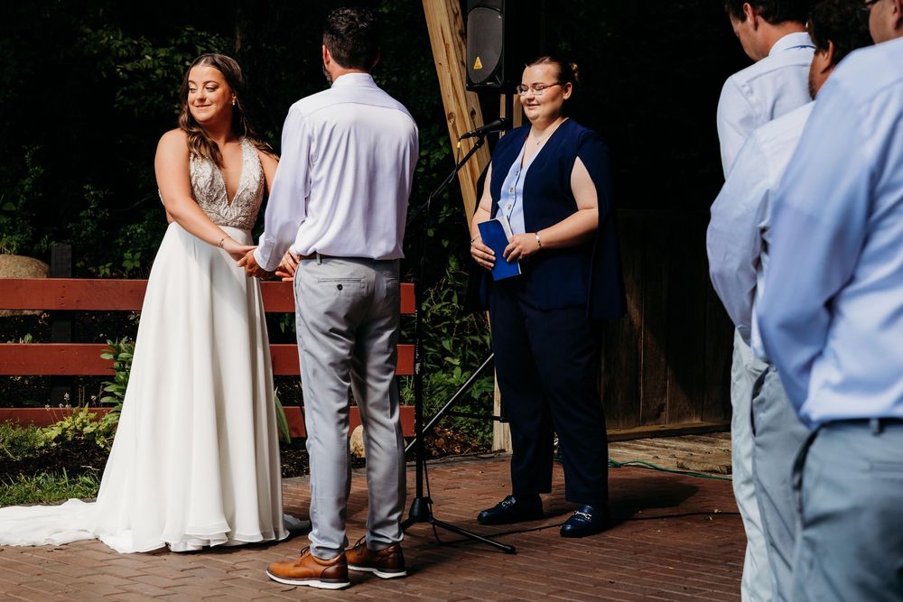 Bride and groom exchange vows outdoors with officiant during intimate wedding ceremony on brick patio.