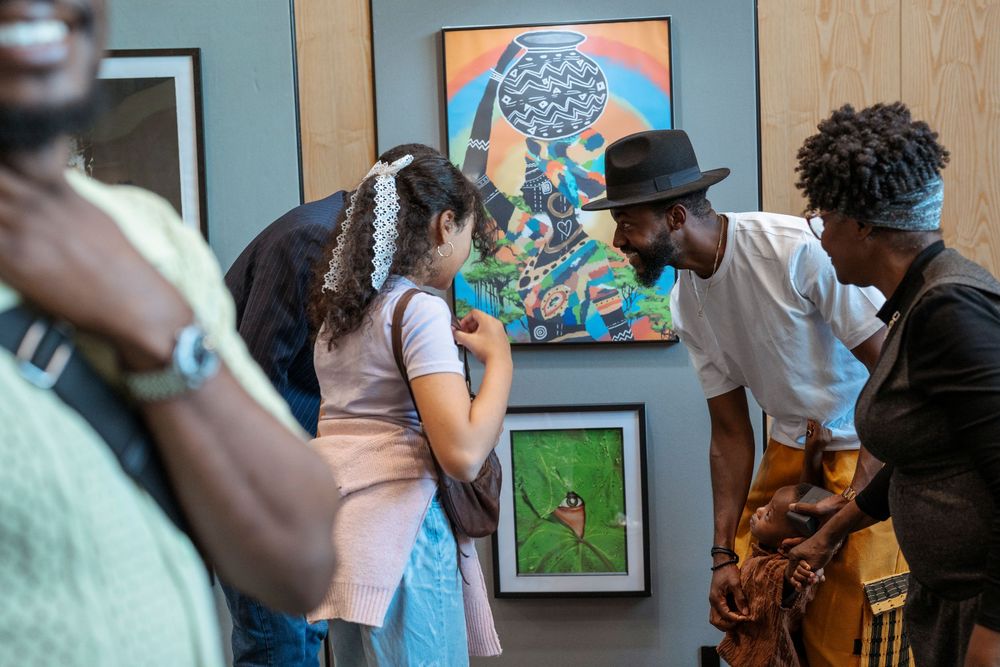 People viewing colorful artwork at an art gallery exhibition, engaging with paintings on display.