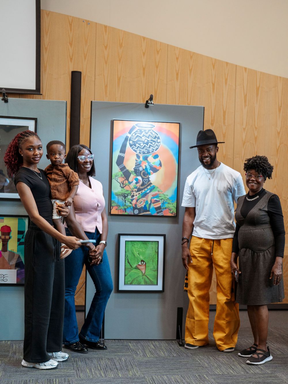 Group of five people posing together at an art gallery exhibition with colorful paintings displayed behind them.