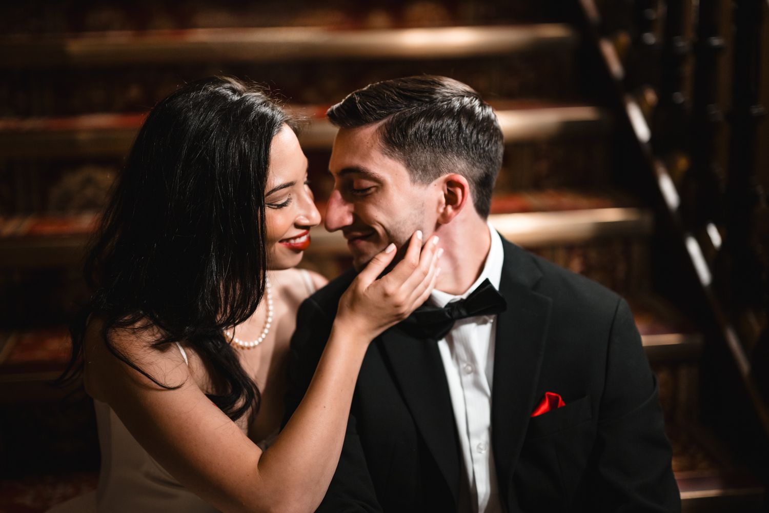 Couple in formal attire sharing a tender moment, woman in white dress touching man's face in black tuxedo.