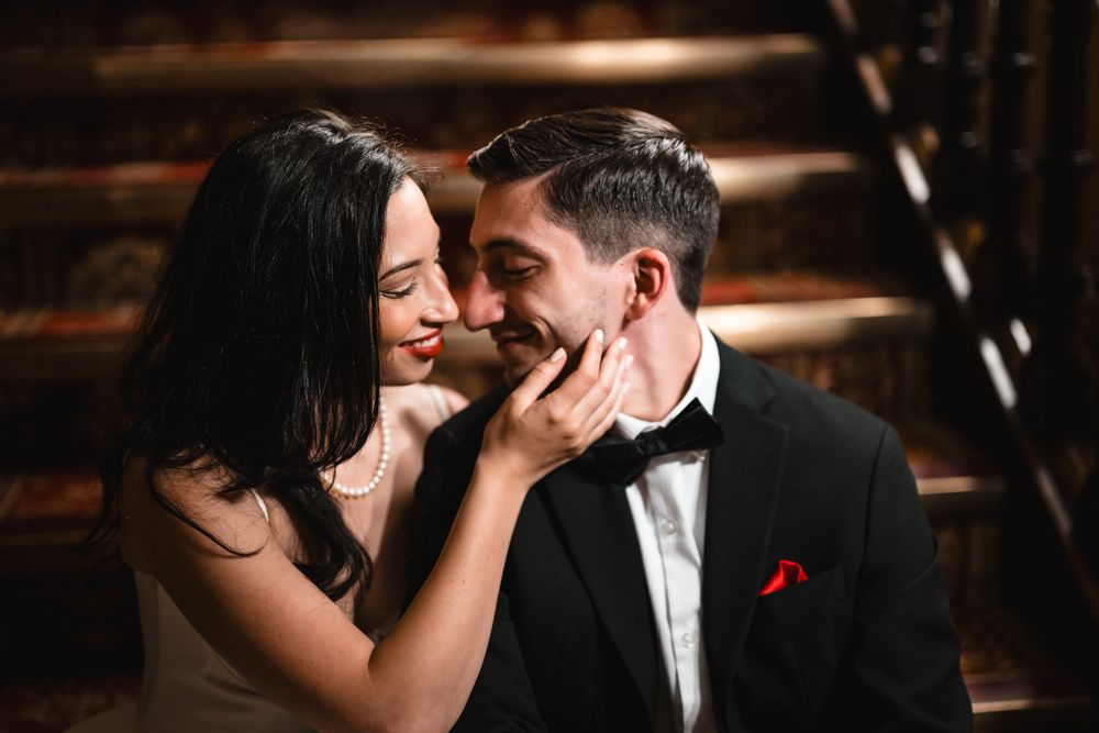 Couple in formal attire sharing a tender moment, woman in white dress touching man's face in black tuxedo.