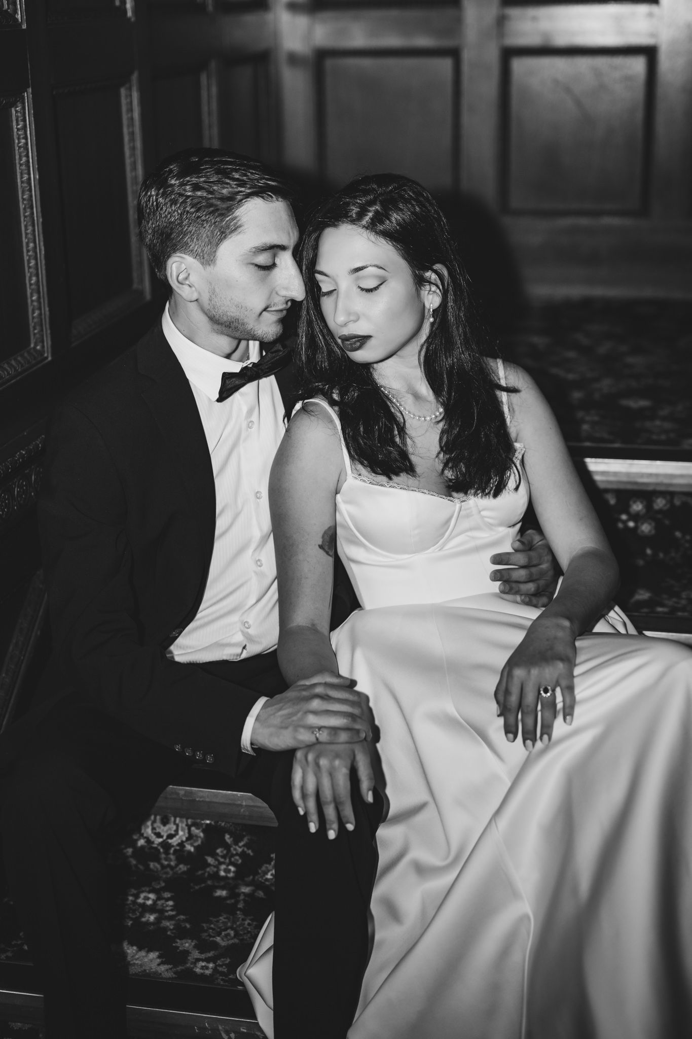 Black and white photo of an elegant couple in wedding attire, bride in white gown and groom in tuxedo, sharing intimate moment.