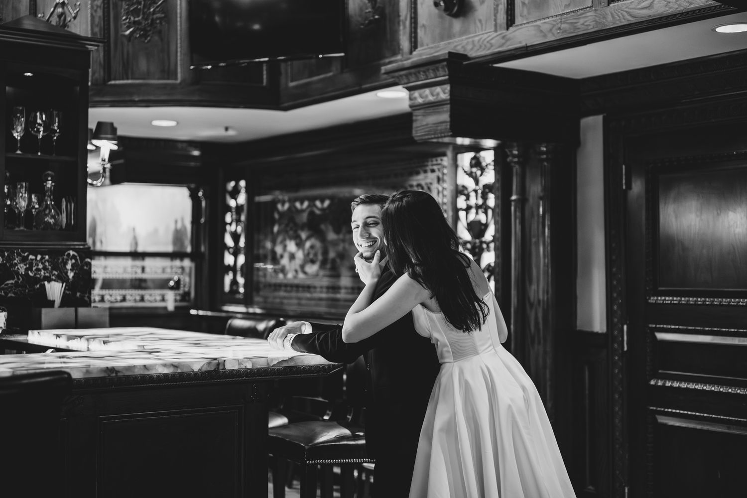 Black and white photo of a bride and groom sharing an intimate moment at an elegant wooden bar.