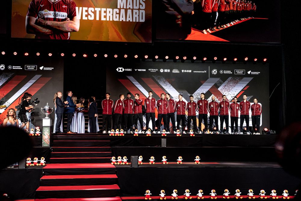 Maus Vestergaard team presentation on stage at a cycling event with athletes in red uniforms under dramatic lighting.