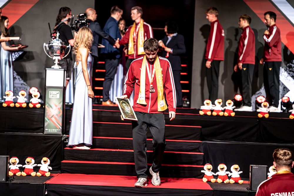 Athletes in red and gold uniforms descend stairs at a formal awards ceremony with trophies and decorations.