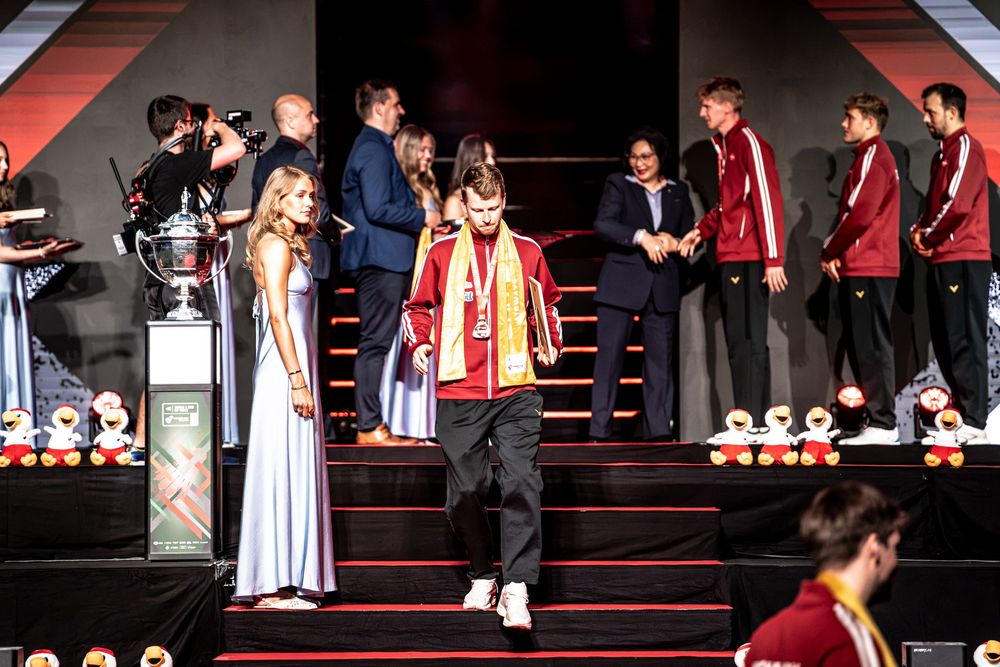 Athletes in red uniforms on a ceremonial stage with a trophy during an awards ceremony event.