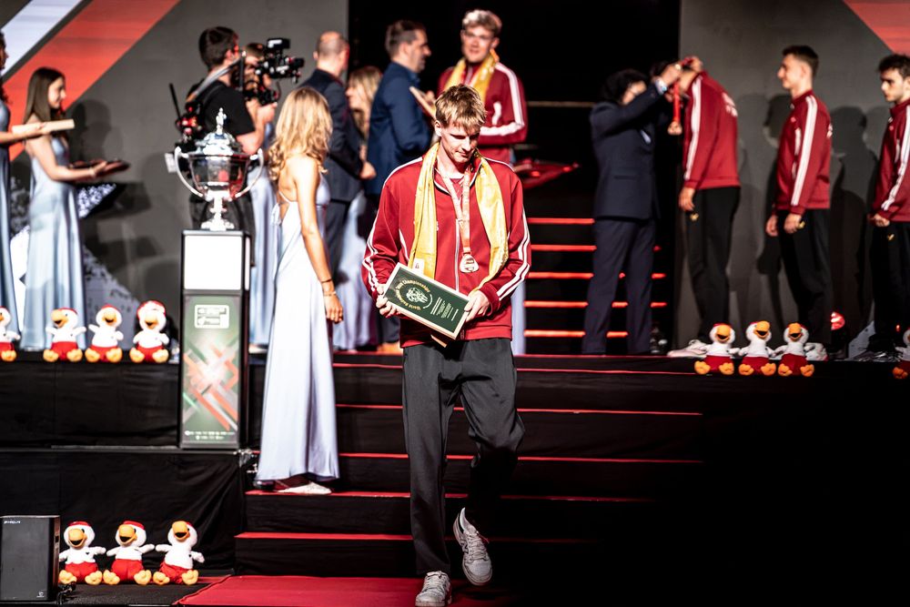 A young male athlete walks down stairs holding a trophy plaque at a formal sports awards ceremony.