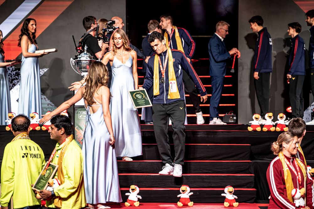 Athlete receives award on stage with medals and trophies at a badminton championship ceremony.